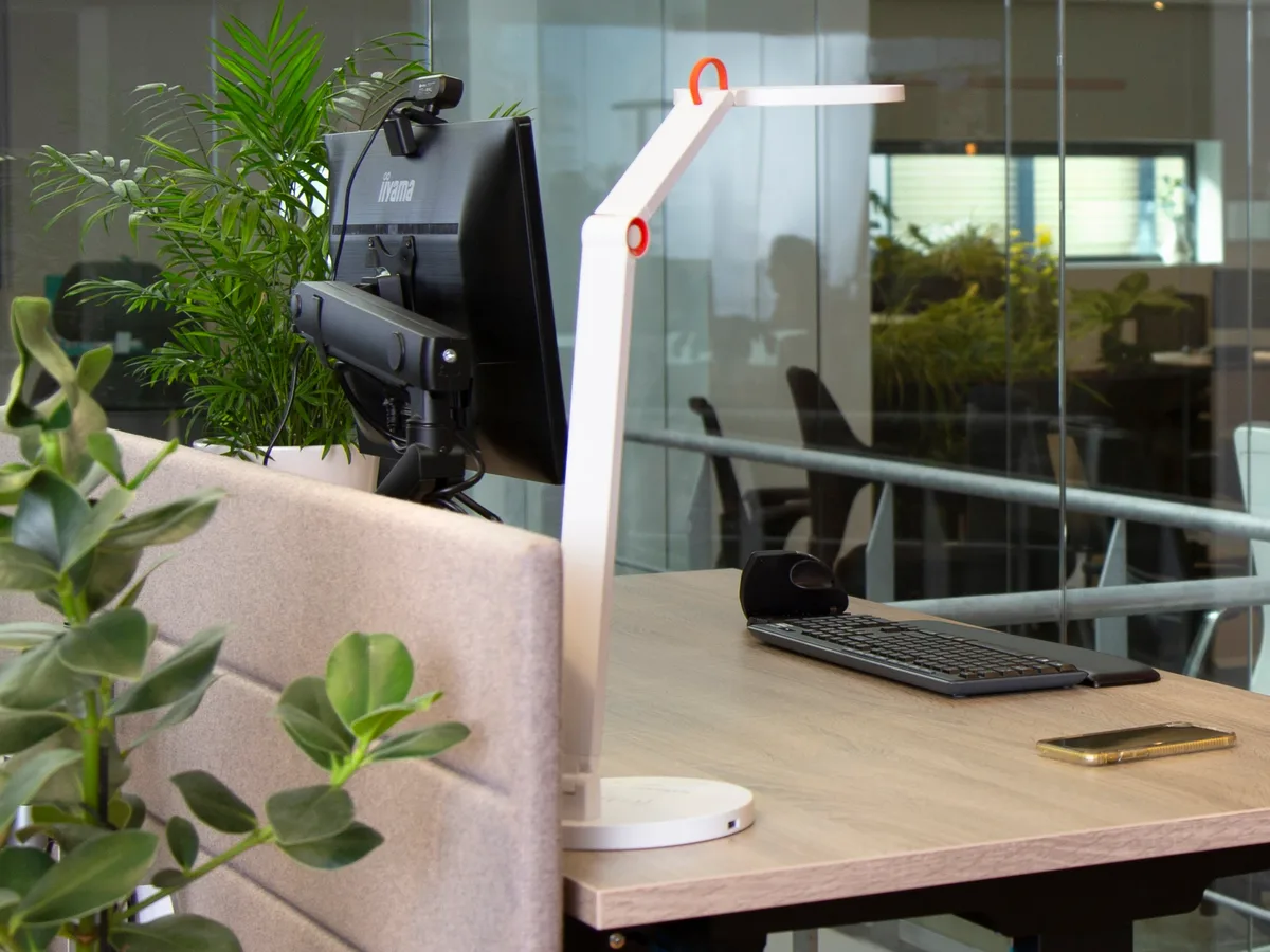 Een goed afgestelde werkplek met monitorarm, bureaulamp en akoestisch scherm